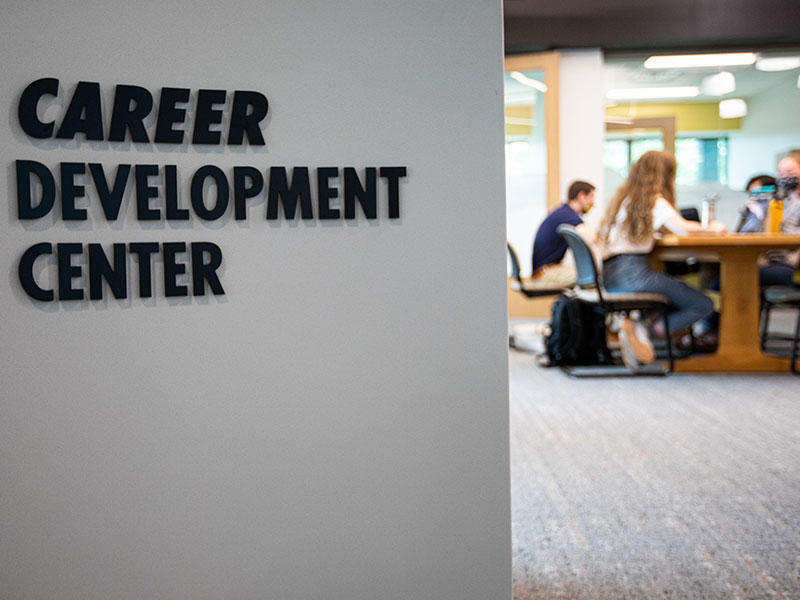 A wall sign reading ‘Career Development Center’ with students meeting at a table in the background.