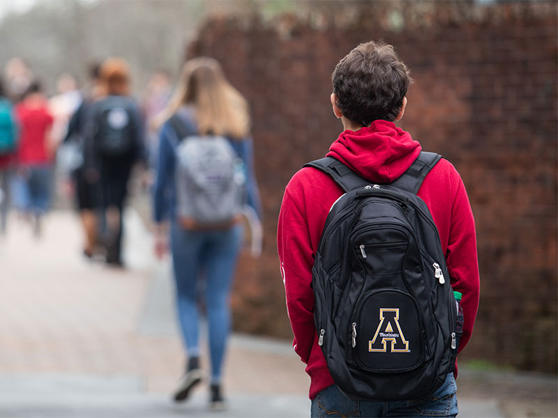 A student wearing a backpack walks along a campus path with others ahead.